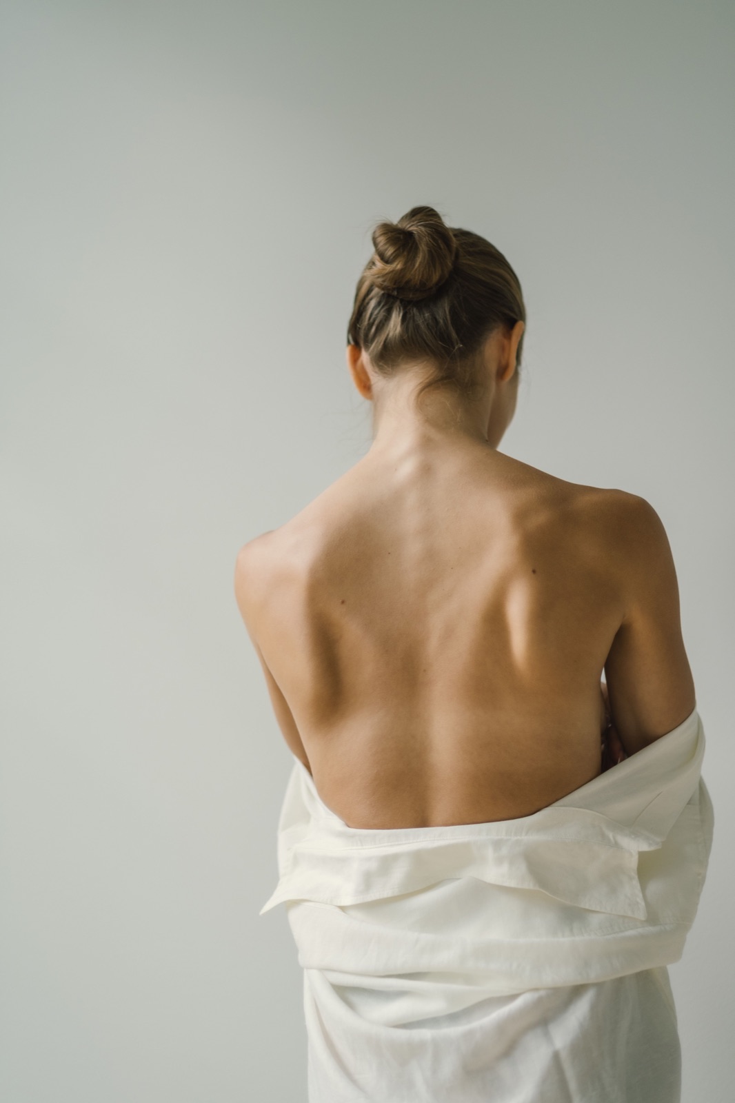 Woman seated with her back visible against a plain wall